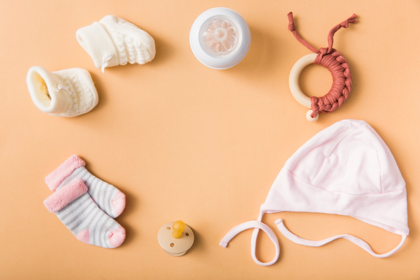 baby-s-sock-pair-woolen-shoes-pacifier-cap-milk-bottle-toy-orange-background